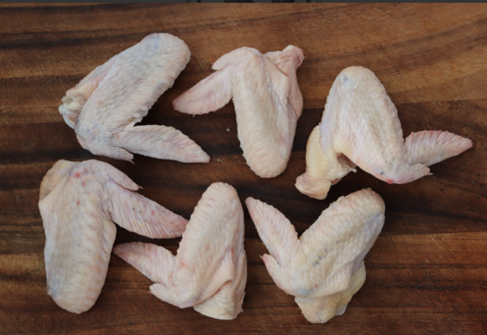 Raw Sommerlad heritage chicken wings arranged on a wooden board, six intact pieces.
